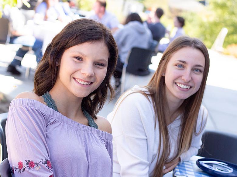two girls at picnic table during a BBQ on the patio smile for photograph