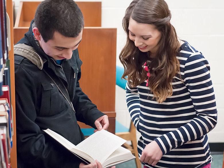 two new students look at a book in the library