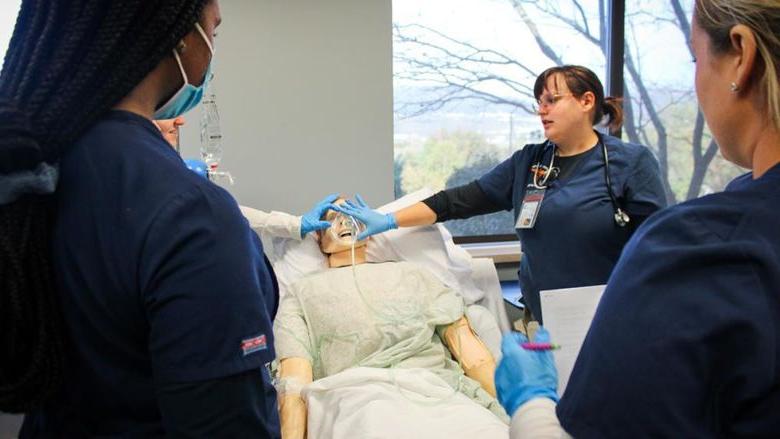 专业护士和学生护士聚集在校园病人模拟器实验室的病人模拟器周围.