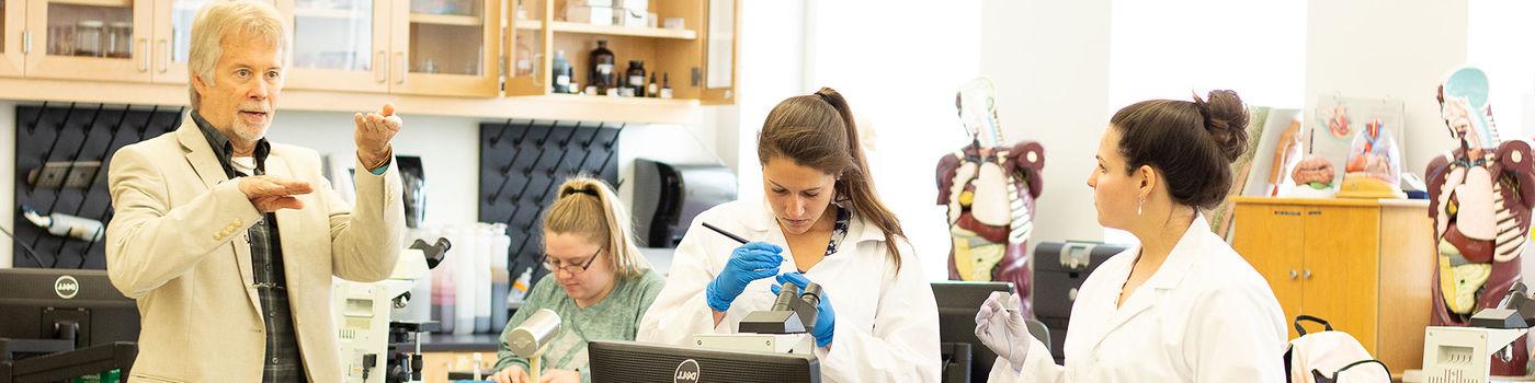 获得生物学学位的学生和他们的教授穿着实验服在生物实验室里