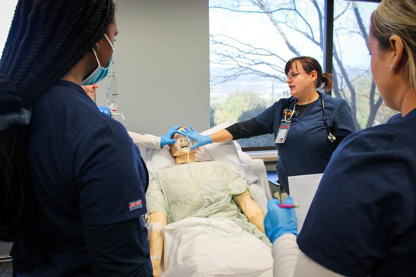 专业护士和学生护士聚集在校园病人模拟器实验室的病人模拟器周围.